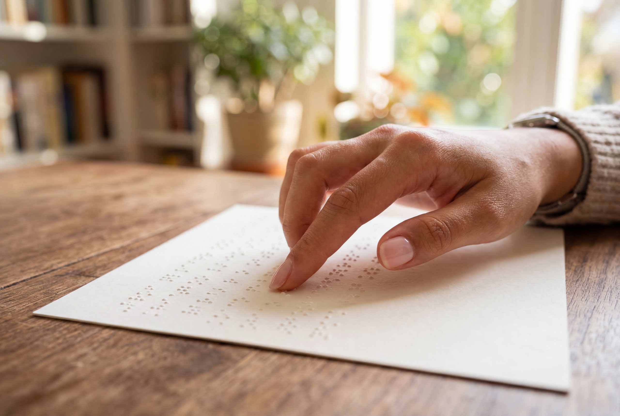 Hand reading a document written in braille on a wooden table Hand reading a document written in braille on a wooden table