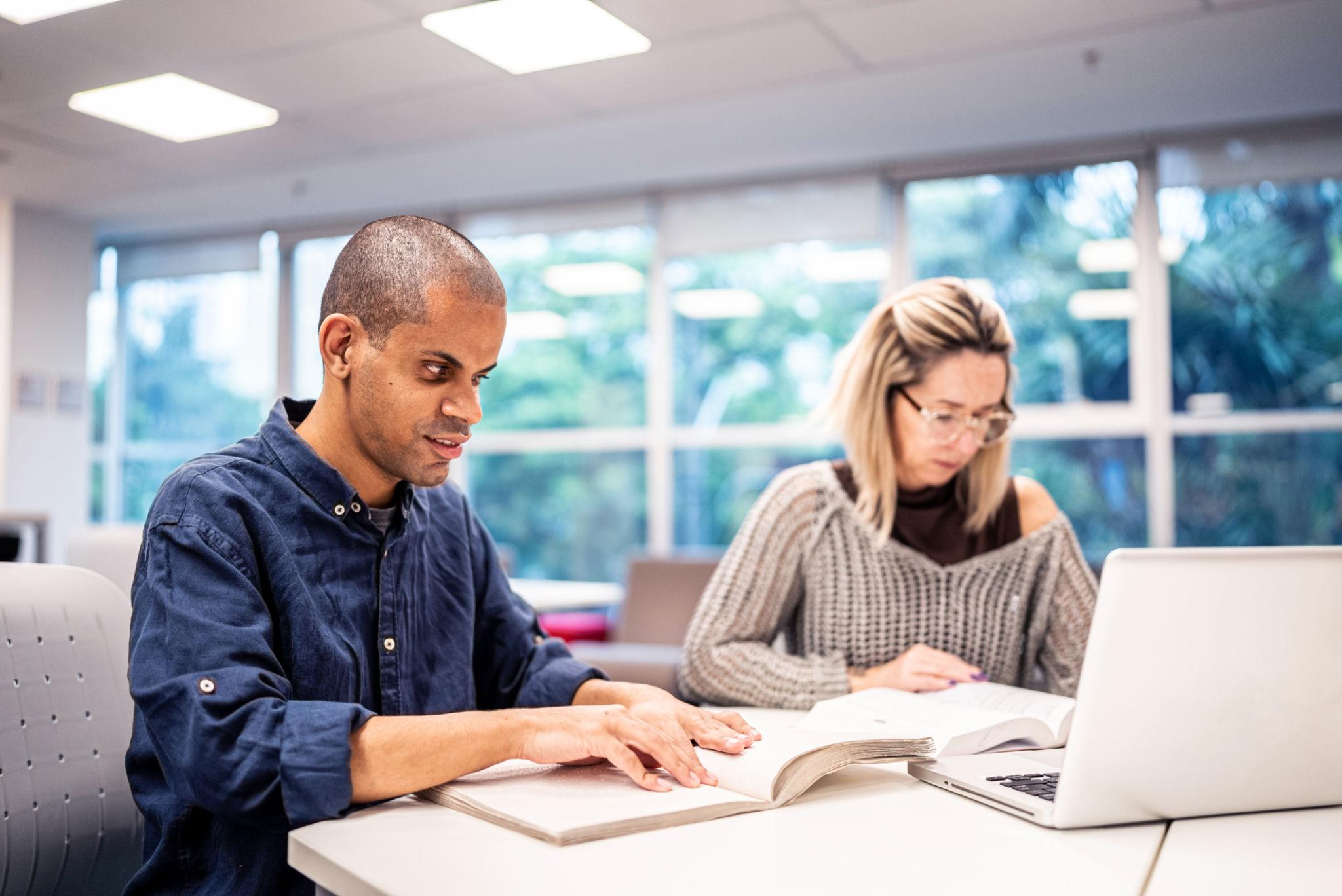 Mid adult man visually impaired man reading a braille book at university